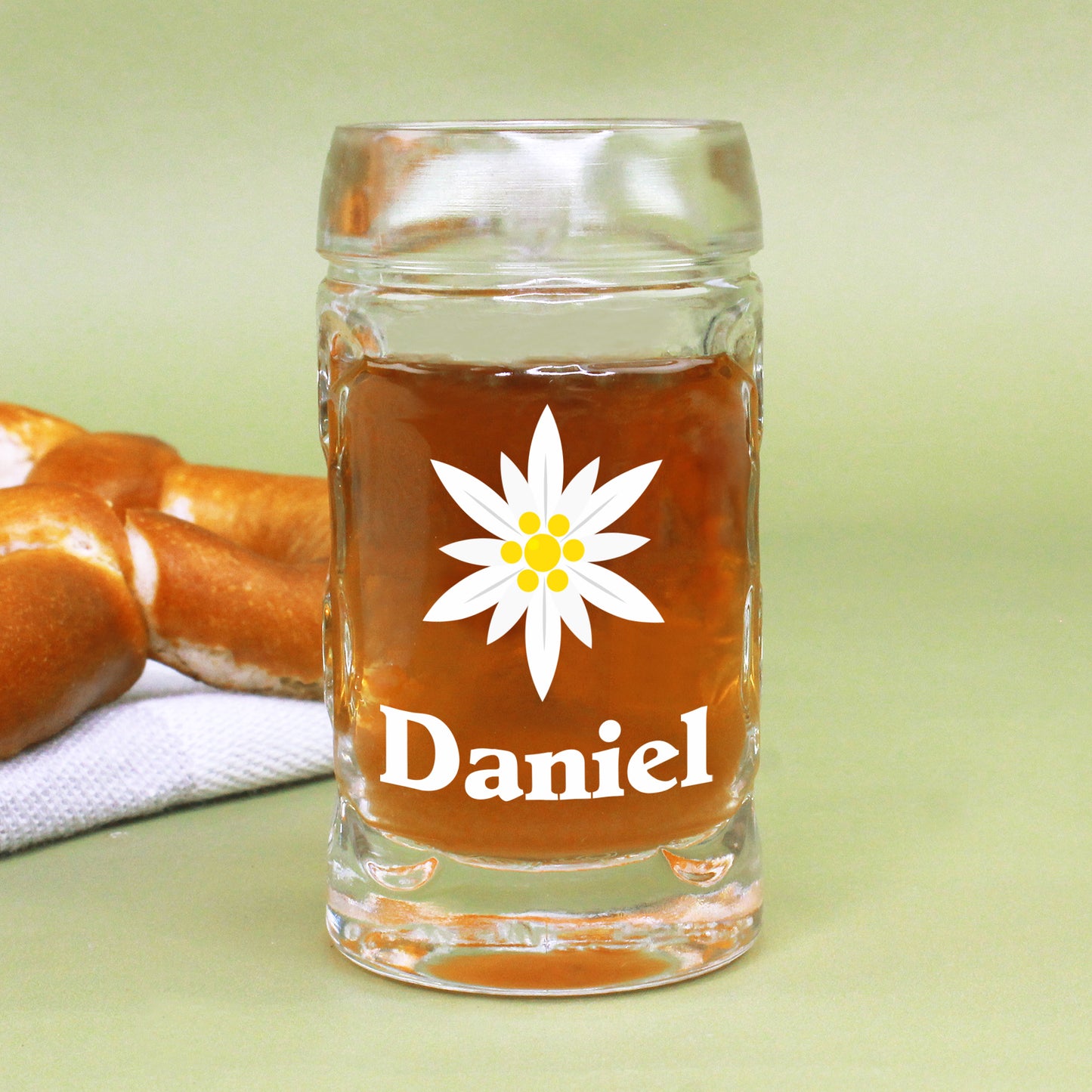 Mini-Bierkrug mit Edelweiß-Aufdruck und Name Daniel – vor Brezel auf grünem Untergrund