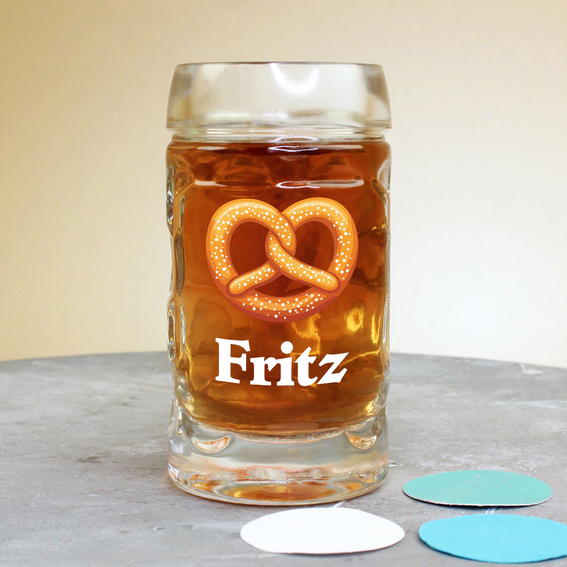 Mini-Bierkrug (4 cl) mit Brezel-Motiv und Name Fritz, stehend auf Tisch mit buntem Konfetti