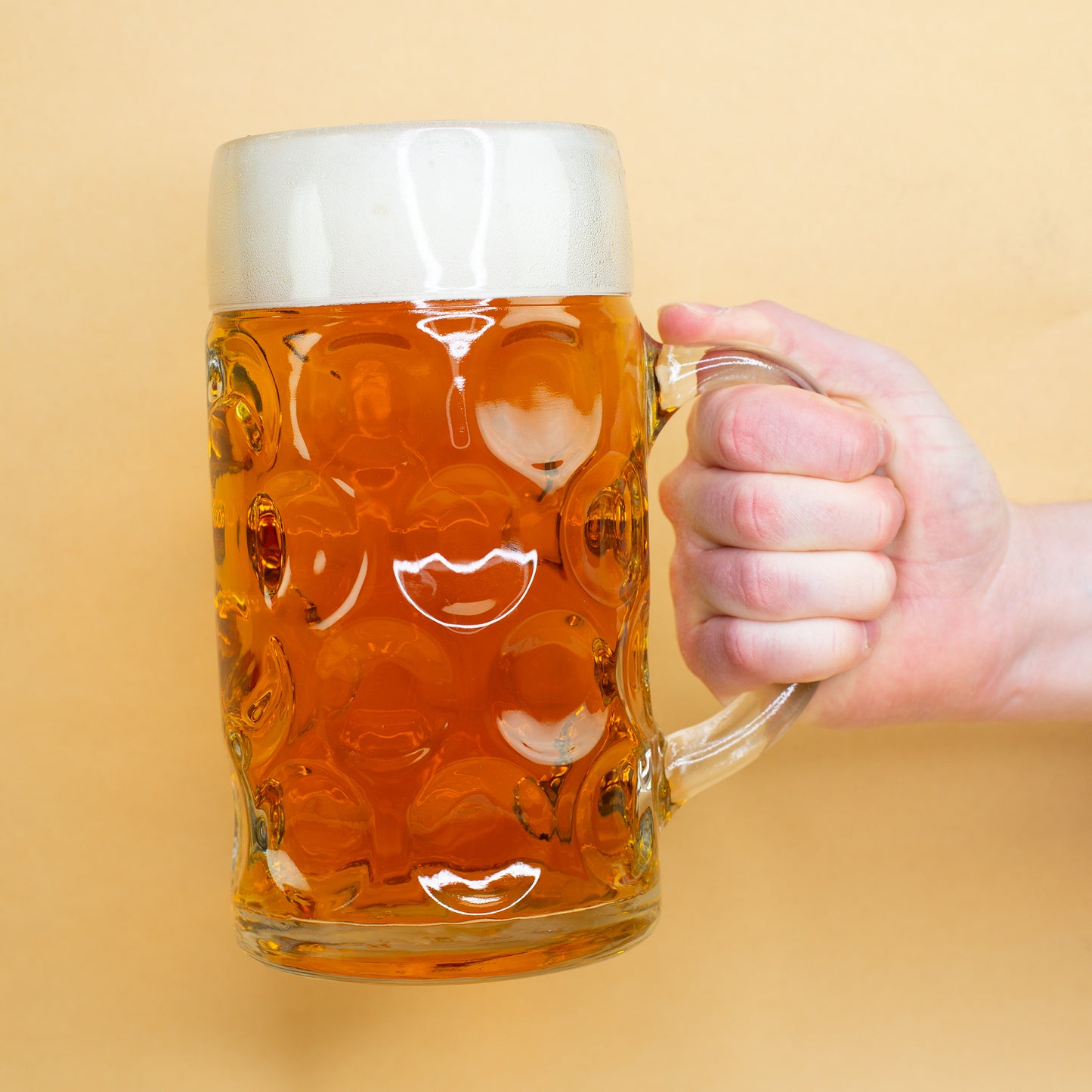 1-Liter-Maßkrug in Hand gehalten, ohne Motiv, seitliche Ansicht vor gelbem Hintergrund