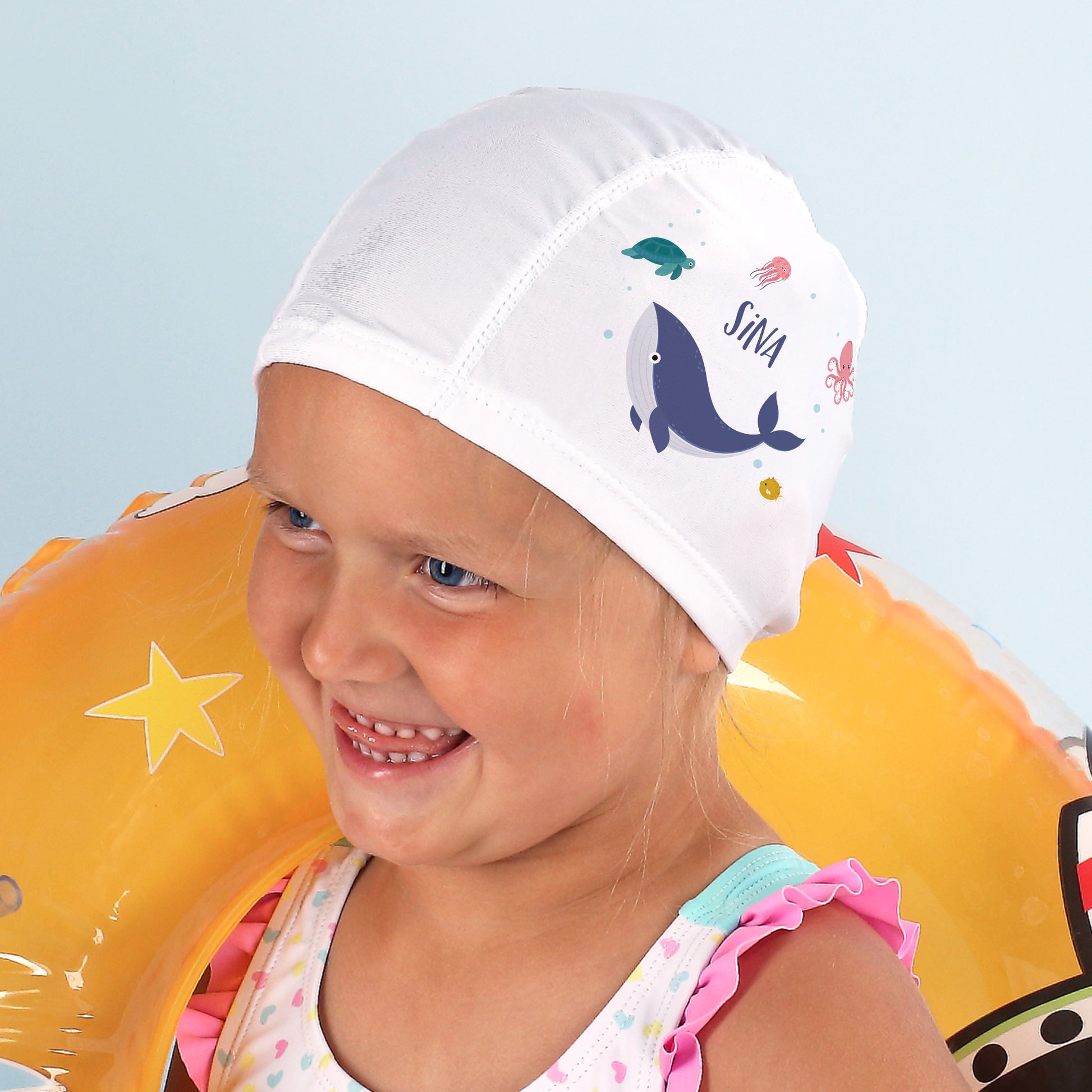 Mädchen mit gelben Schwimmflügeln trägt Badekappe mit Wal-Design