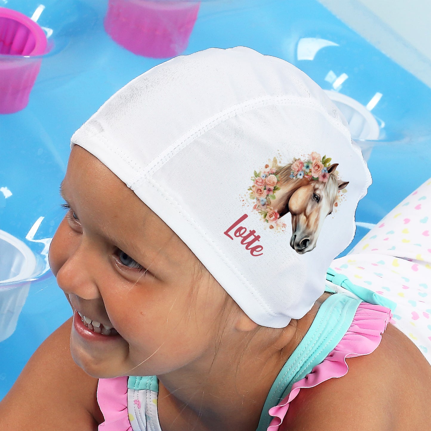Mädchen trägt Badekappe mit Pferdemotiv und Name „Lotte“ am Pool