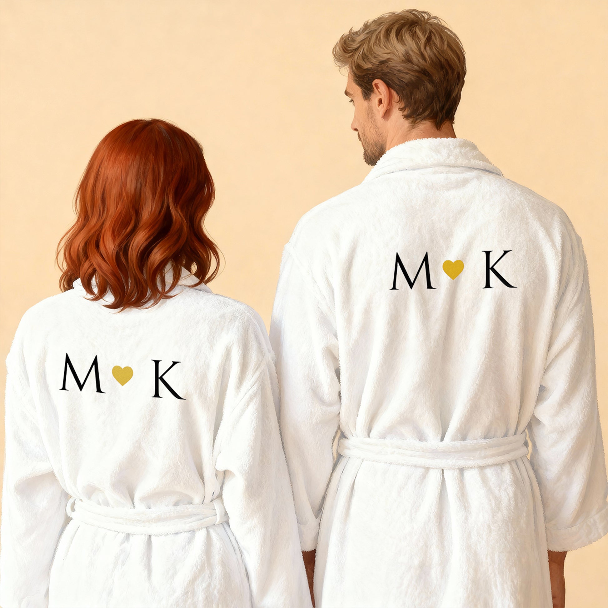 Zwei weiße Bademäntel im Partnerlook mit gestickten Initialen und goldenem Herz auf dem Rücken, Paar von hinten