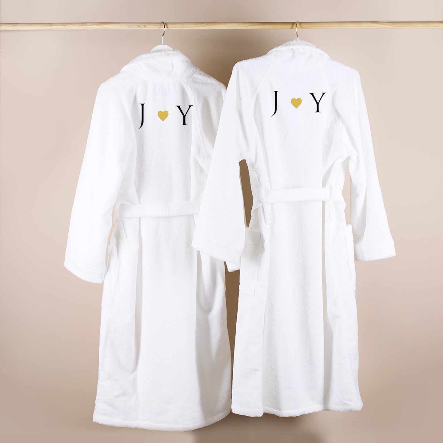Zwei weiße Bademäntel auf Kleiderbügeln, bestickt mit Initialen und goldenem Herz, Partner-Bademantel Set