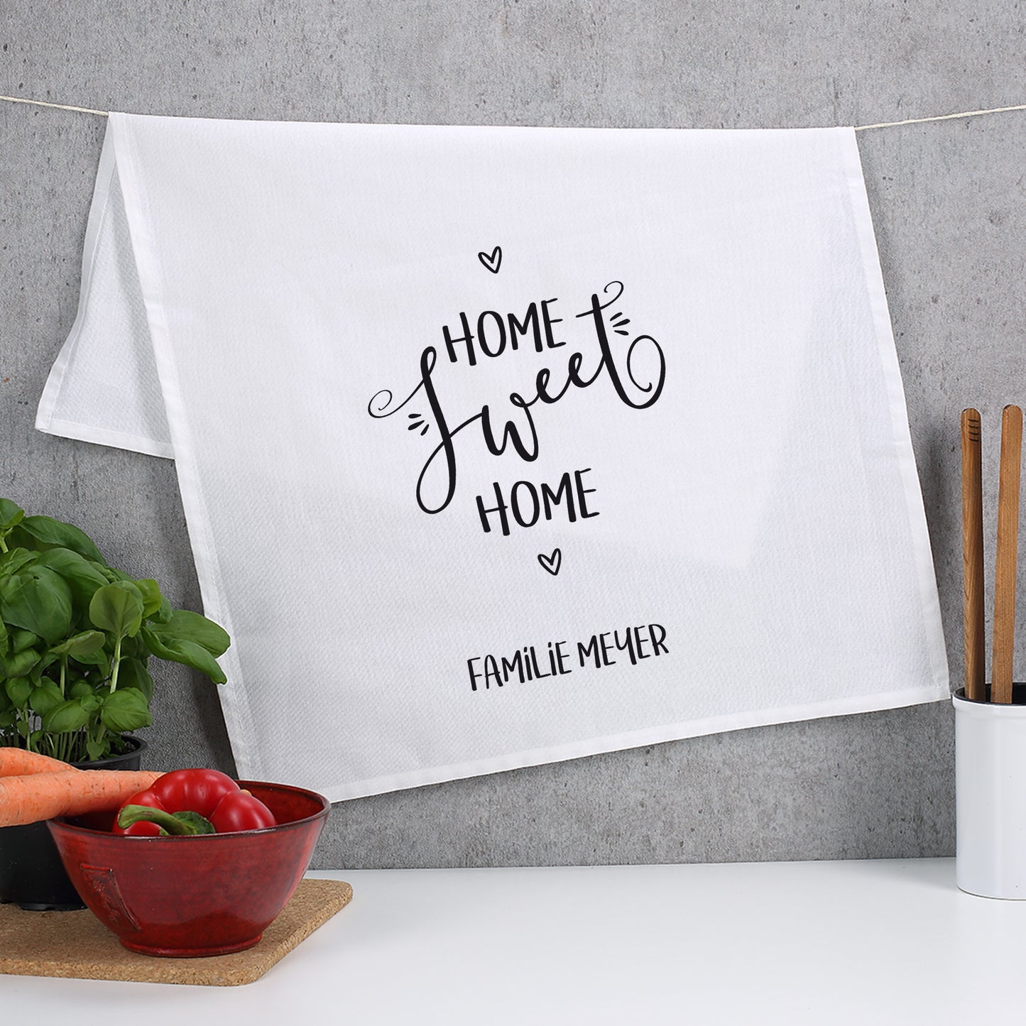 Küchentuch mit „Home sweet Home“ und Familienname Meyer, aufgehängt vor grauer Wand mit Gemüse