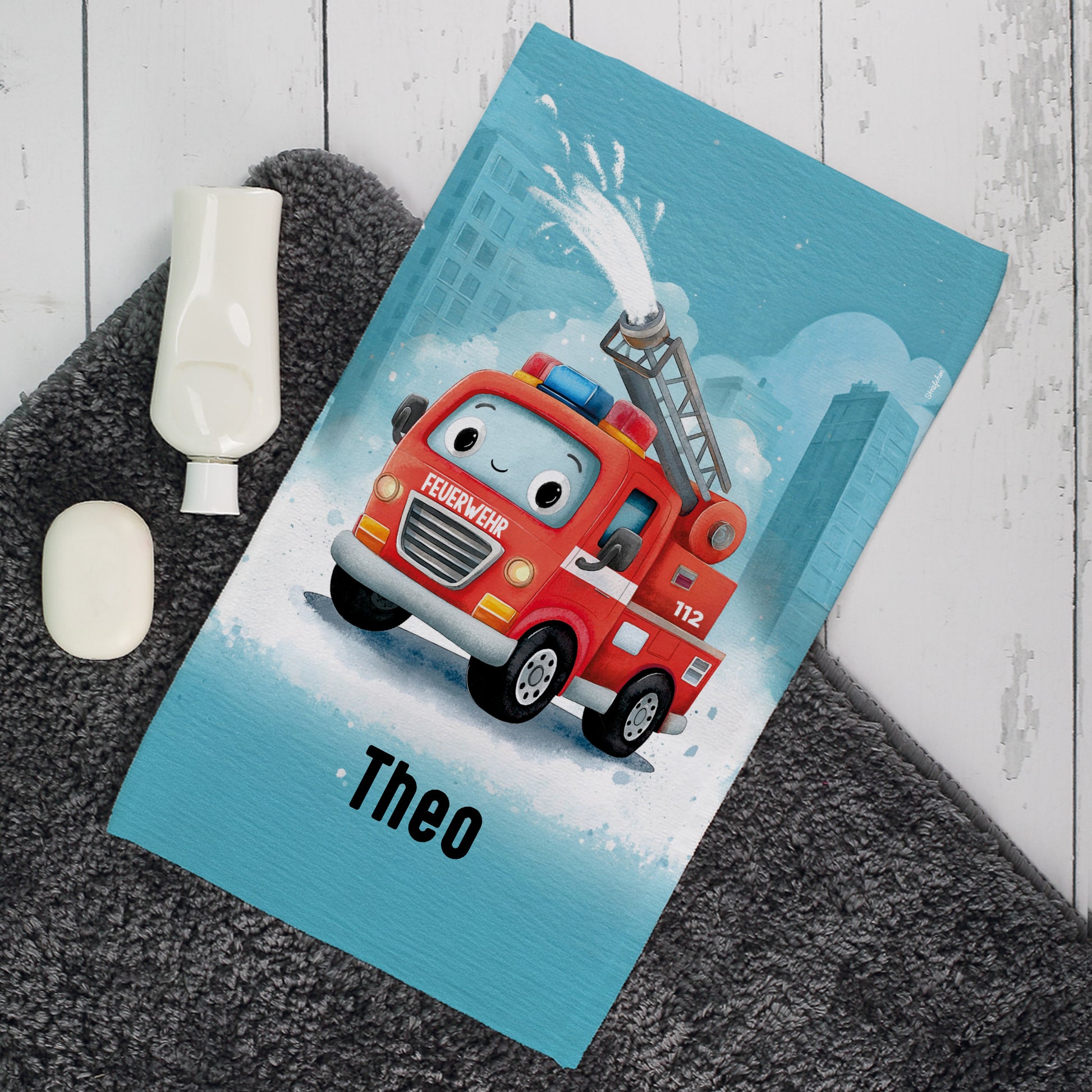 Personalisiertes Kinderhandtuch mit Feuerwehrauto Motiv und Name Theo auf grauem Badteppich