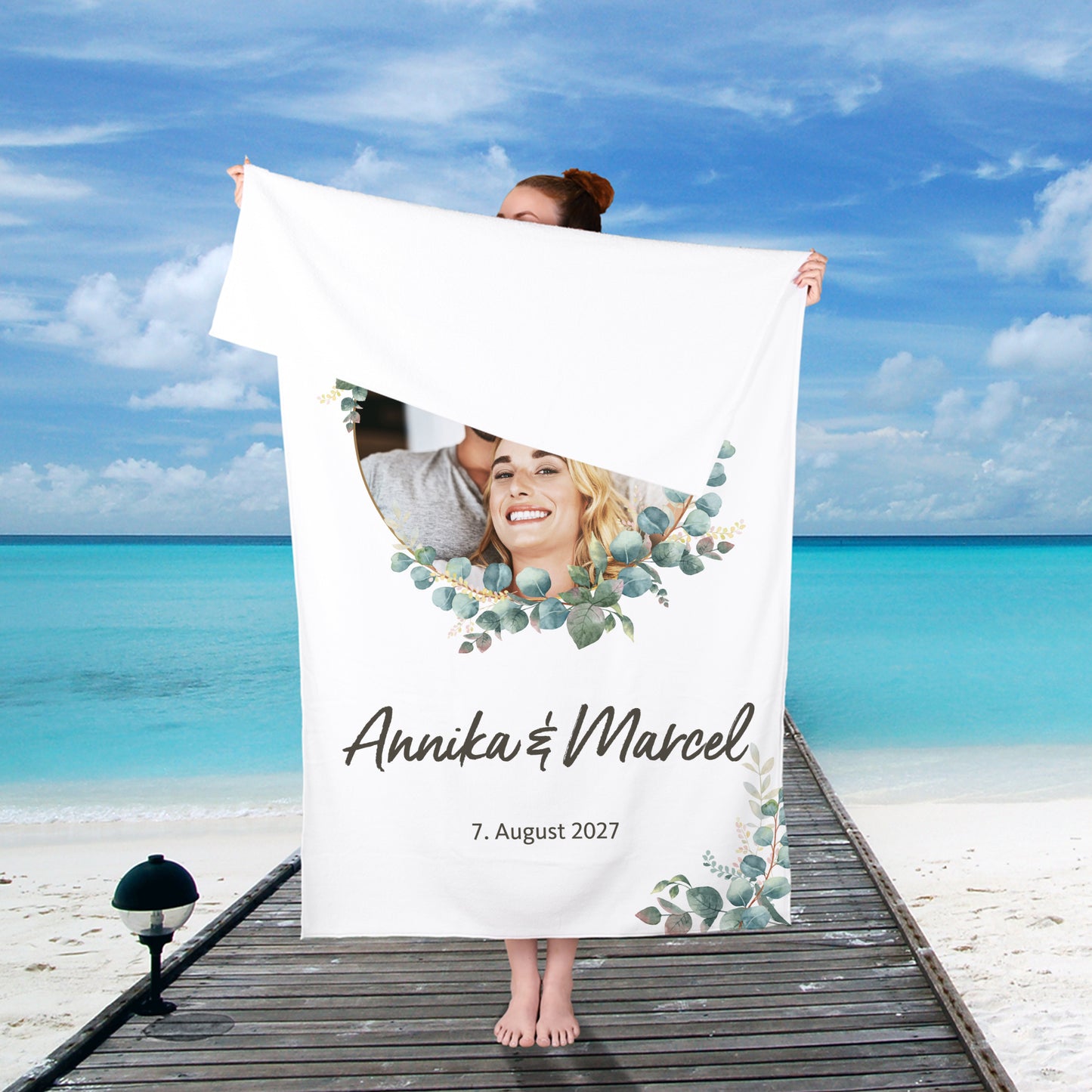 Hochzeits-Handtuch mit Eukalyptus-Motiv, personalisiert mit Foto, Namen und Wunschtext – von einer Person am Strand gehalten.