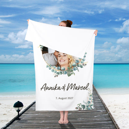 Hochzeits-Handtuch mit Eukalyptus-Motiv, personalisiert mit Foto, Namen und Wunschtext – von einer Person am Strand gehalten.