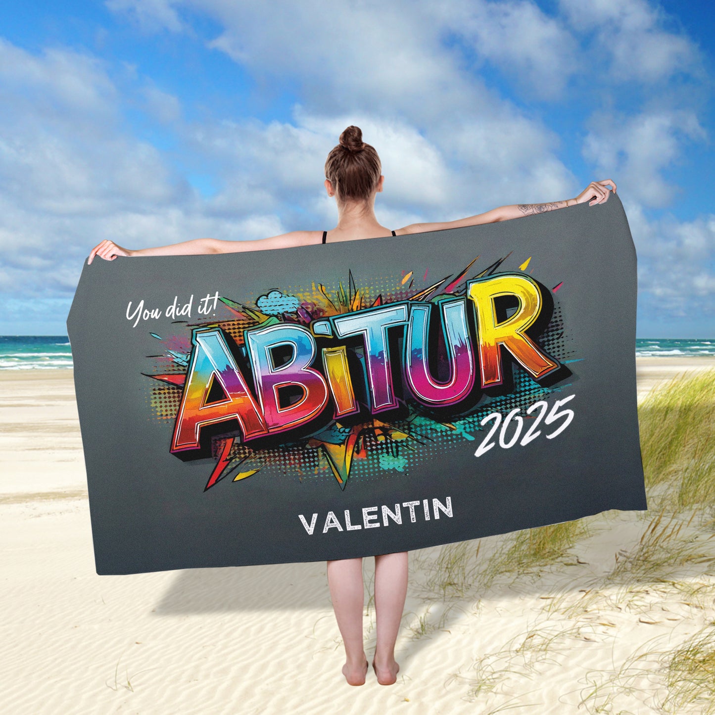 Person zeigt das personalisierte Abitur-Handtuch im Querformat ausgebreitet – bunter Graffiti-Druck und Wunschtext gut lesbar.
