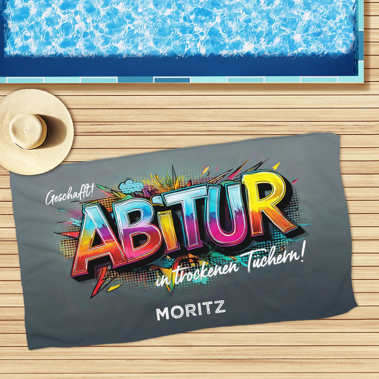 Großes Abitur-Handtuch mit Graffiti-Design am Pool ausgebreitet – sommerliche Kulisse.