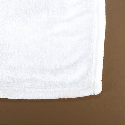 Nahaufnahme der Kuscheldecken-Ecke von hinten, flauschige weiße Rückseite und umnähter Rand auf braunem Untergrund