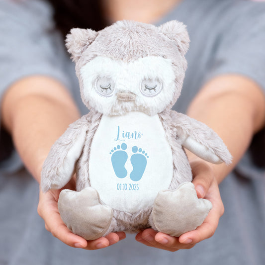 Eine Person hält eine flauschige beigefarbene Kuscheltier-Eule mit geschlossenen Augen in beiden Händen. Auf dem Bauch der Eule sind zwei hellblaue Babyfüßchen sowie der Name „Liano“ und das Geburtsdatum „01.10.2025“ aufgedruckt.