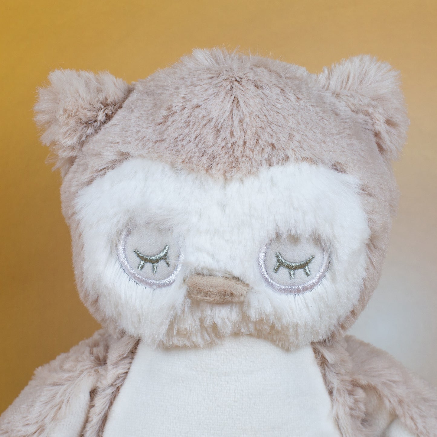 Nahaufnahme des Gesichts der Eule mit geschlossenen Augen, gestickten Wimpern und einem kleinen, beigen Schnabel. Das flauschige Fell ist in hellen Creme- und Beigetönen gehalten.