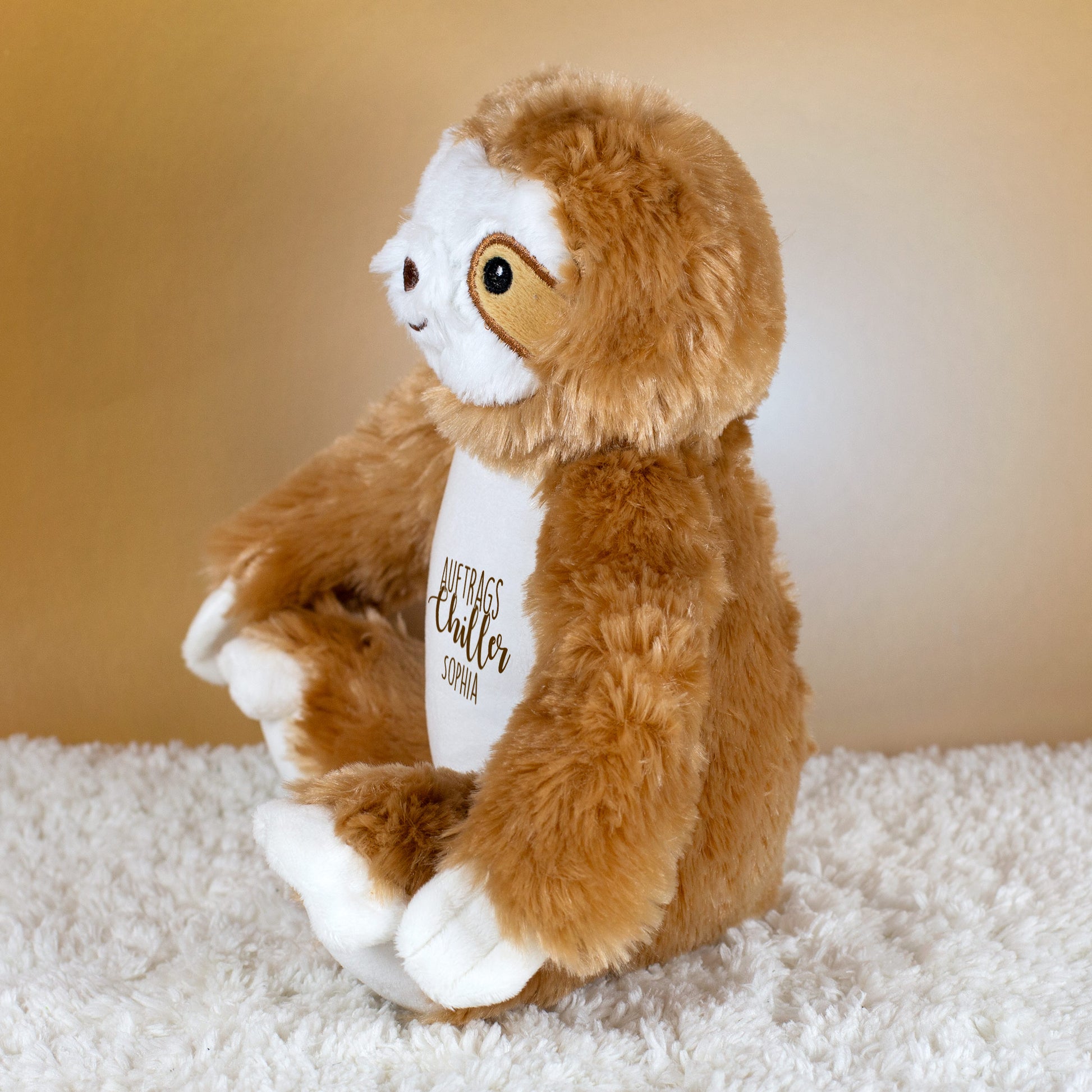 Seitliche Ansicht des weichen Faultier-Kuscheltiers mit Aufdruck „Auftragschiller“.
