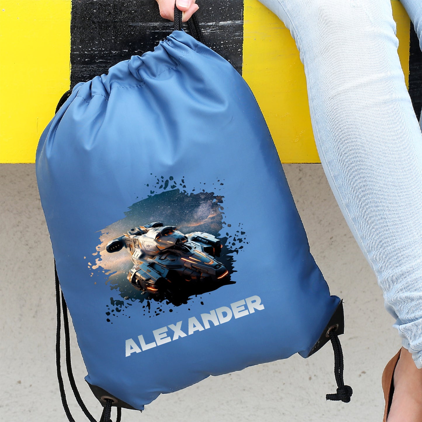Blauer Turnbeutel mit Raumschiff-Motiv und Wunschname „Alexander“, getragen am Geländer