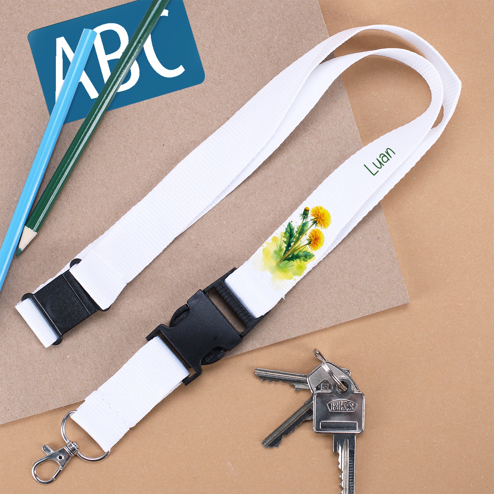 Personalisierter Schlüsselanhänger mit dem Namen "Luan" und Löwenzahn-Motiv, daneben Schlüsseln und Schulmaterial