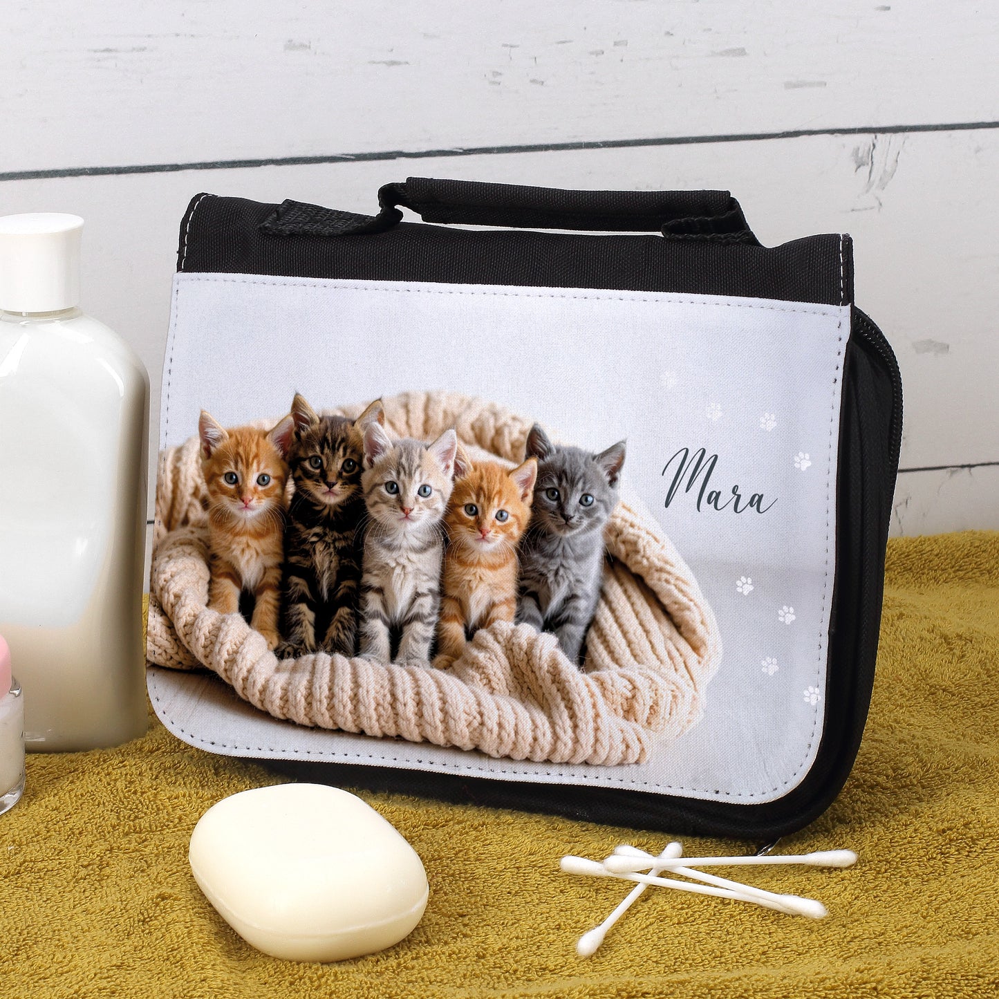 Waschtasche mit Katzenmotiv und Name Mara, geöffnet auf gelbem Handtuch, mit Seife und Lotion