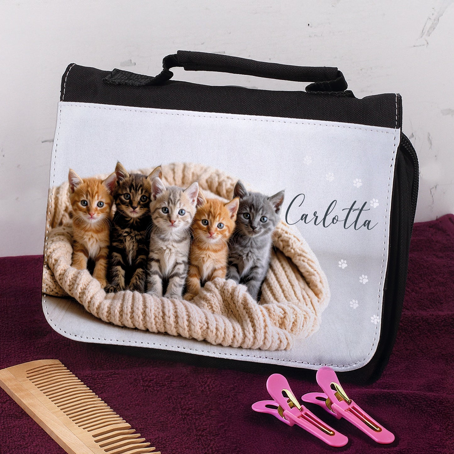 Personalisierte Kulturtasche mit Katzenmotiv und Name Carlotta, auf lila Handtuch mit Haarspangen