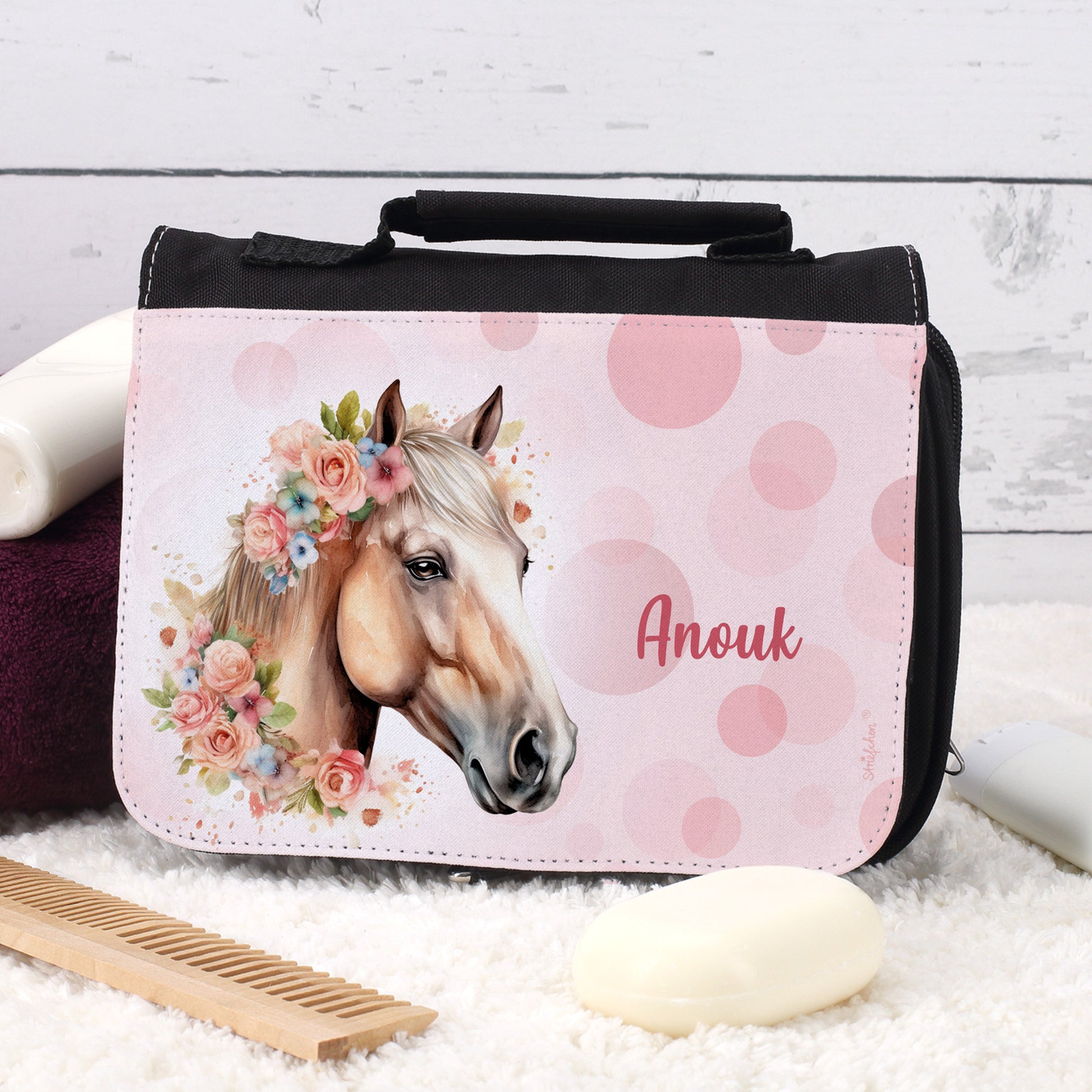 Schwarze Waschtasche mit Blumen-Pferdemotiv und Name „Anouk“ auf Teppich mit Seife und Kamm