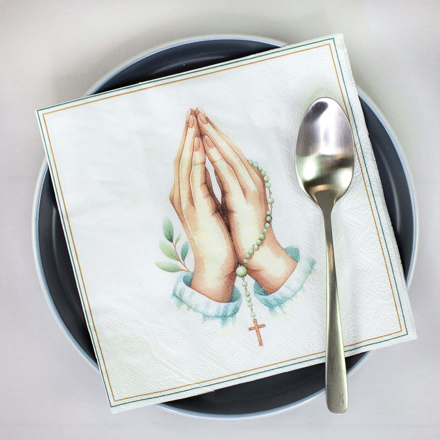 Christliche Serviette mit betenden Händen, Rosenkranz und Kreuz auf einem Teller mit Löffel dekoriert