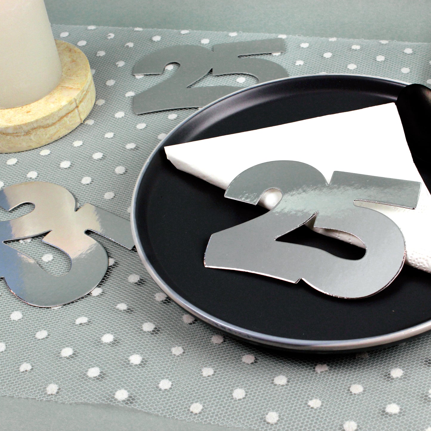 Jumbo-Konfetti Zahl 25 Silber zur Silberhochzeit auf gedecktem Tisch mit Serviette und Kerze