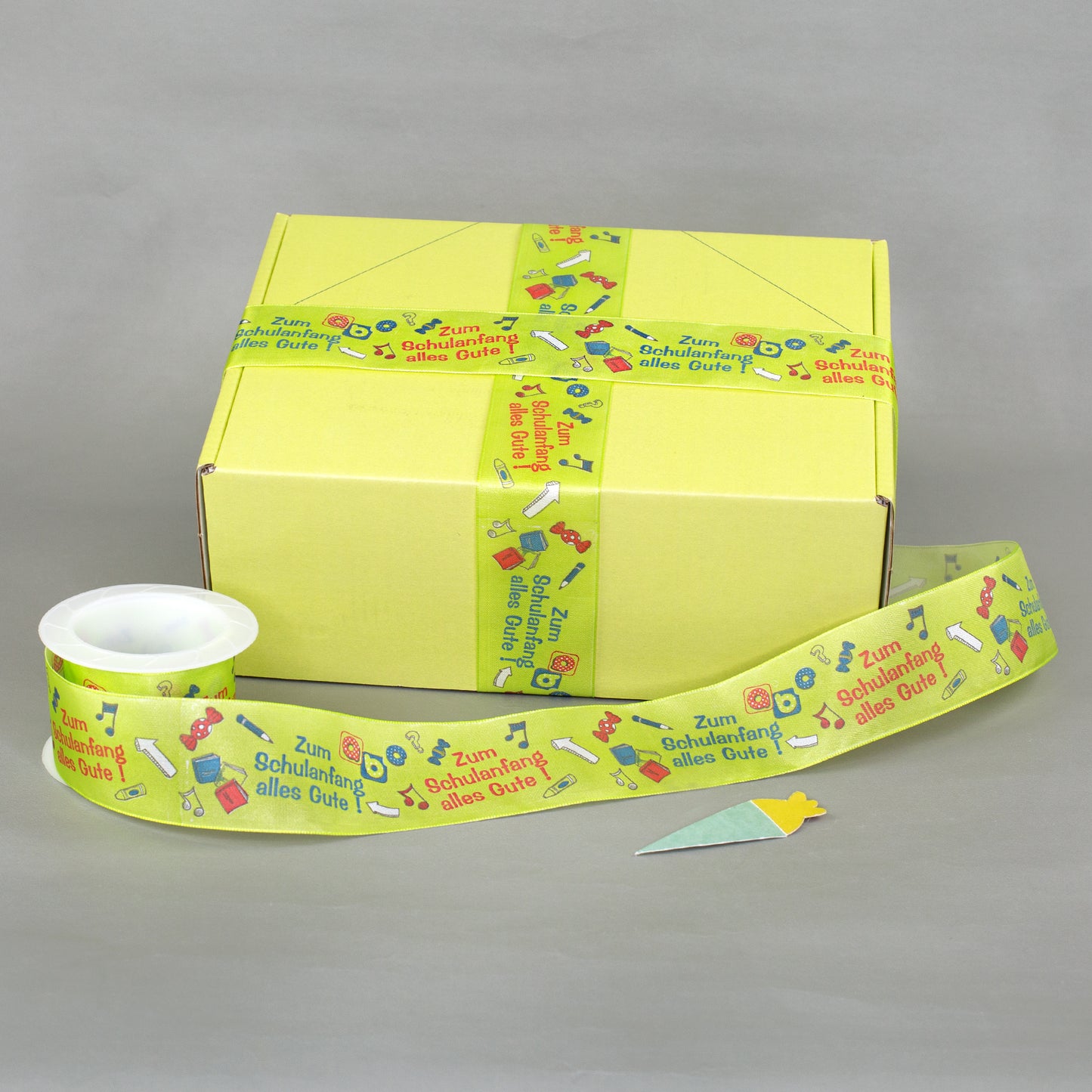Geschenkband zur Einschulung als Dekoration an gelber Geschenkbox mit zusätzlichem Band auf Rolle