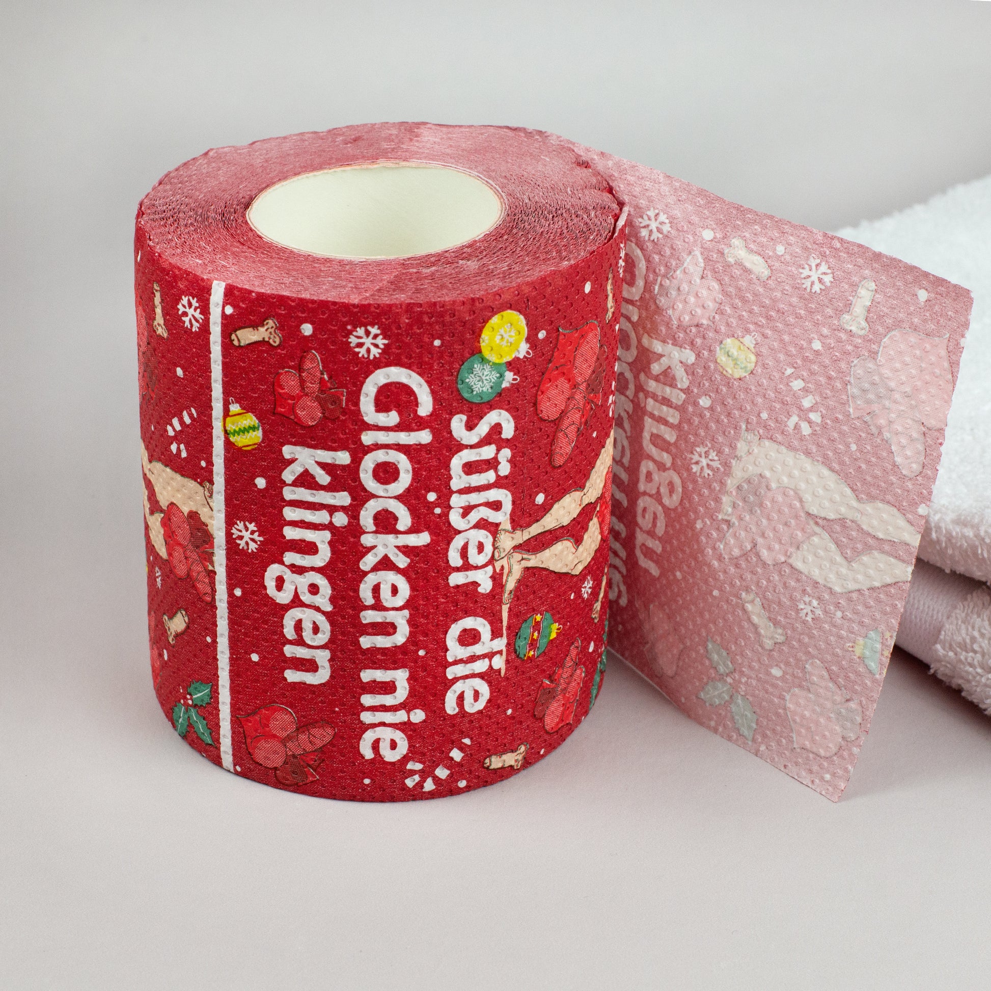 Toilettenpapierrolle Weihnachten rot mit Spruch „Süßer die Glocken nie klingen“ auf weißem Handtuch